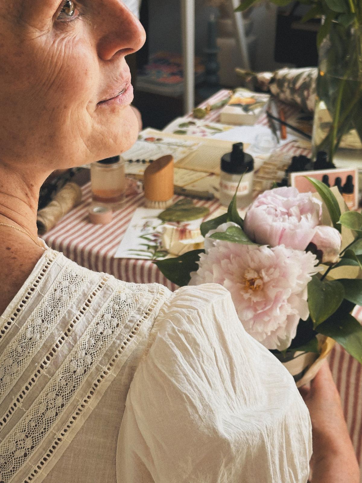 Flavia sostiene peonías rosas junto a la mesa de taller